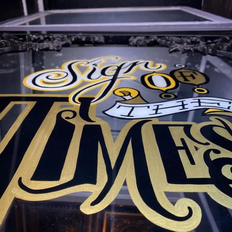 The shop's hand-painted gold-leaf sign on the studio glass, reading Sign of the Times in ornate lettering.